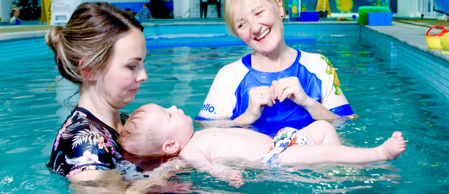 woman helping baby float on its back in pool