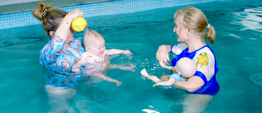 woman holding baby in pool and pouring water on head