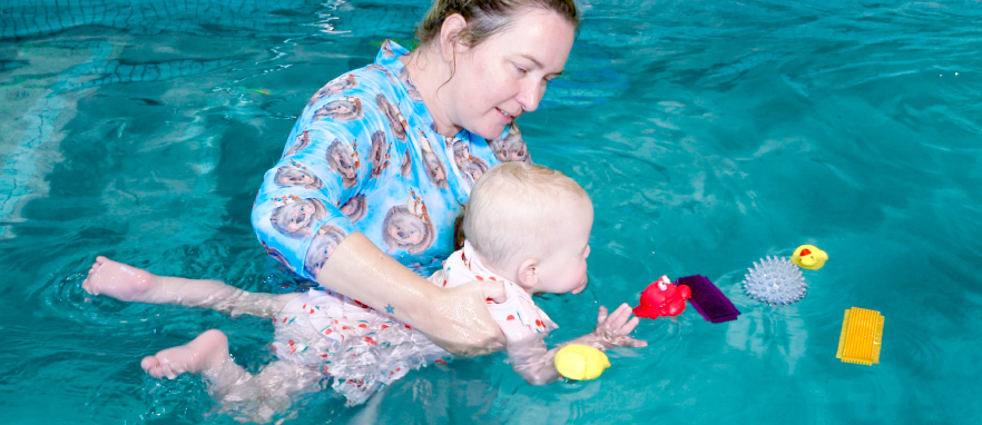 woman helping baby swim forward in pool