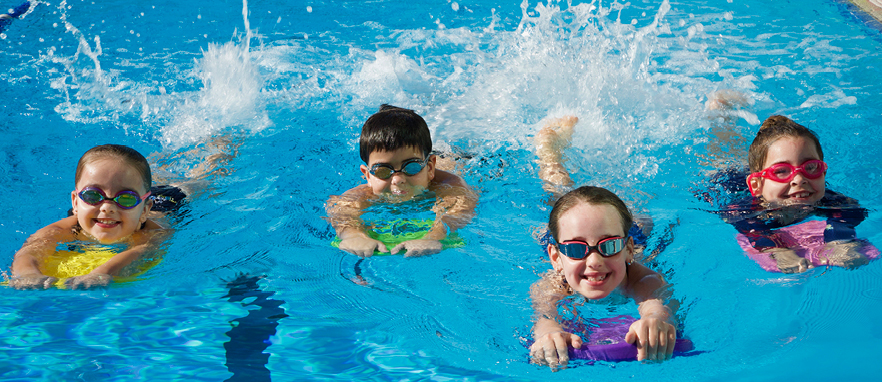 4 small children smiling and practising swimming in the pool with the help of floatation devices