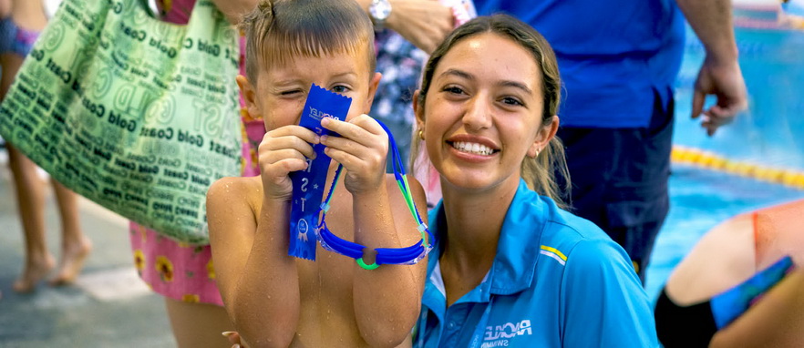young boy just out of the swimming pool holding a medal with a smiling young lady next to him
