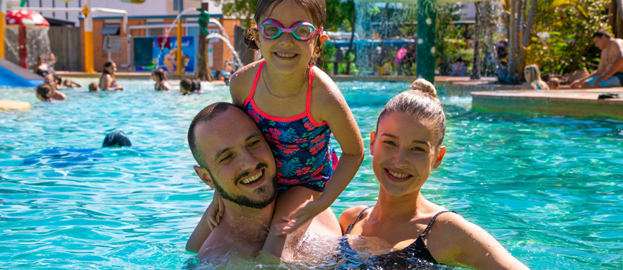 young couple in pool with daughter on mans shoulders